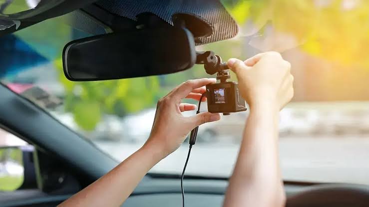A dash cam being positioned on the windscreen beside the rear-view mirror